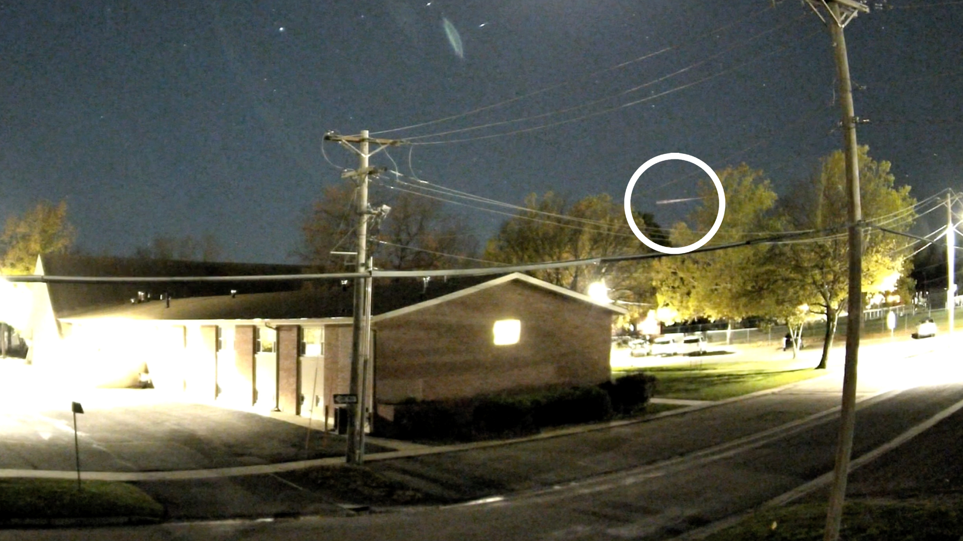 a streak of fire is visible in the night sky above the rooflines of houses in a residential neighborhood